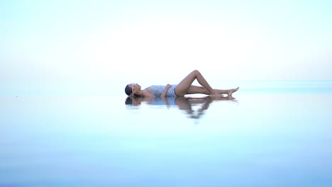 a woman lies on her back in the shallow end of an infinity-edge pool giving the illusion she is floating in midair