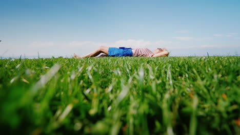 the green lawn on which the young woman lies looks at the sky and has a rest