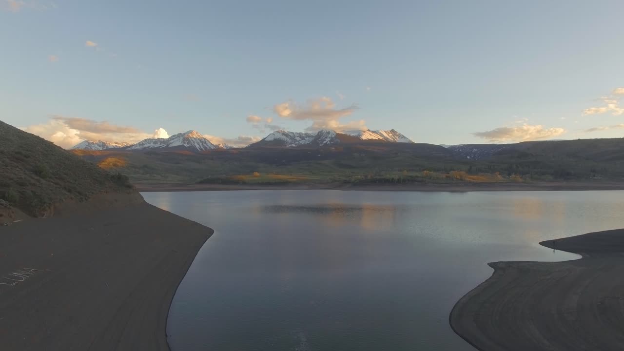 красивый снимок заката, бушующего над горным склоном на фоне заснеженных скалистых гор и озера