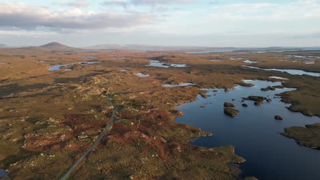 wide aerial shot of connemara lakes with calm lakes in the foreground and beanna beola mountain range in the distance, slowly descending aerial shot