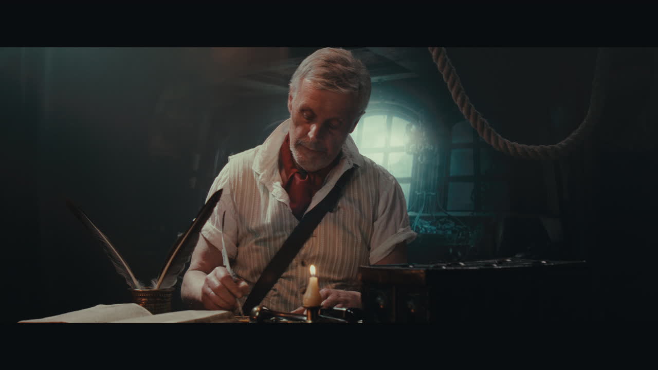 An old captain sits writes a letter inside the sailing ship cabin