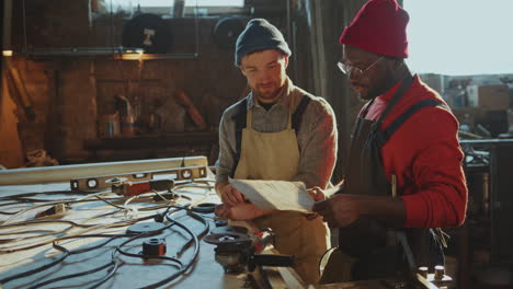 two male colleagues discussing metalwork drawing in blacksmith workshop