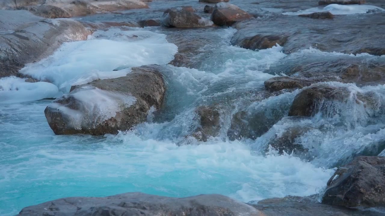 Cascata blu che scorre tra le rocce con pezzi di ghiaccio accanto.