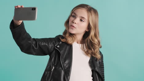una adolescente caucásica con chaqueta de cuero tomando selfies con su teléfono inteligente.