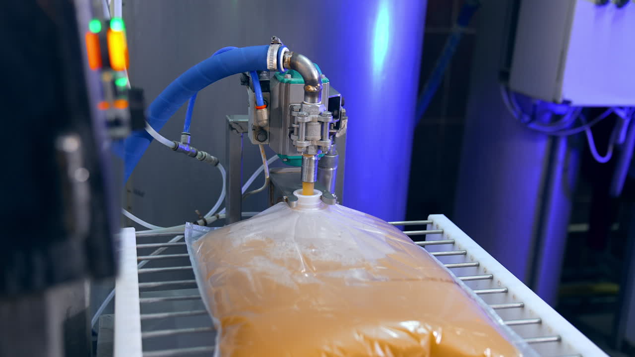 Big transparent plastic bag is filled with organic juice from the automatic machine. Apple juice manufacturing at the plant. Close up.