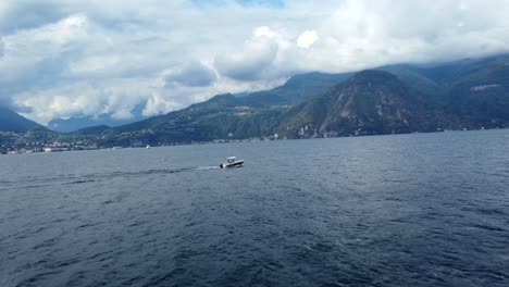 Drone-shot-of-boat-sailing-on-water-of-Lake-Como-with-Alps-in-Italy