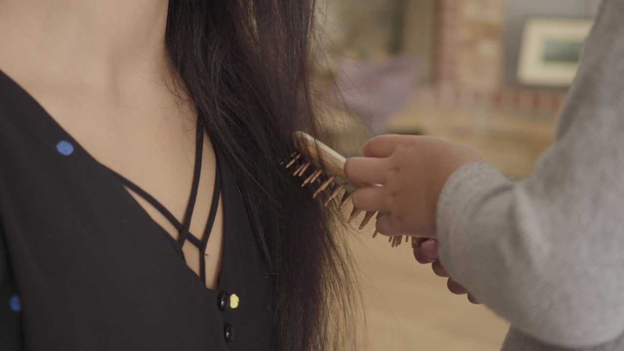 Close-up of child's hands brushing the smiling Middle Eastern woman with long dark hair and hazel eyes