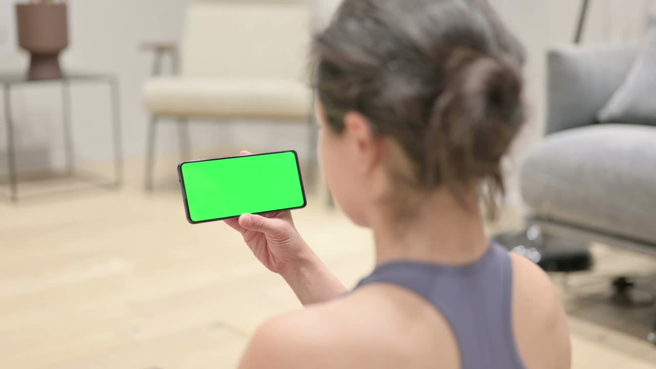 vista trasera de una mujer india usando un teléfono inteligente con pantalla cromada en una alfombra de yoga