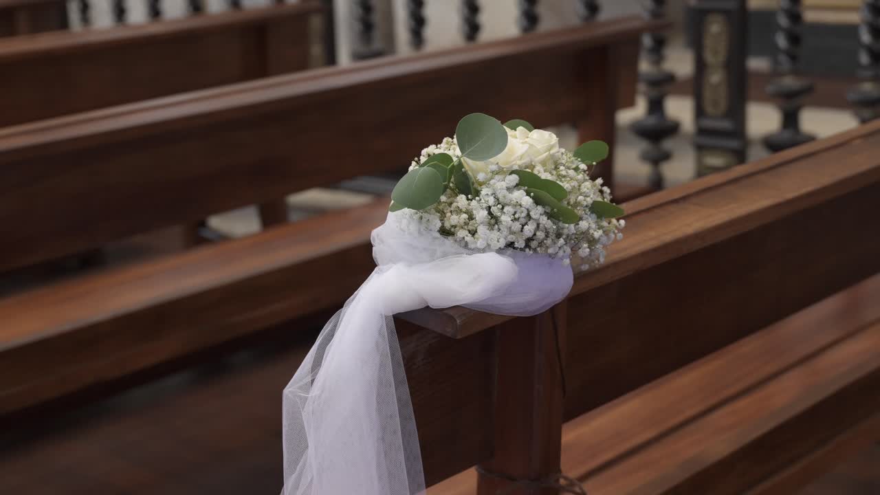 delicata disposizione floreale con rose bianche e il respiro del bambino legato con un tessuto bianco su un banco di chiesa in legno, preparato per una cerimonia nuziale