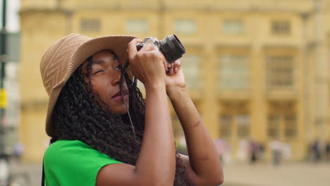 female tourist wearing straw sun hat with camera on vacation in oxford uk exploring city walking along broad street taking photos