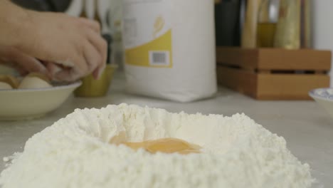 chef puts egg yolk into flour ring on kitchen cooking table