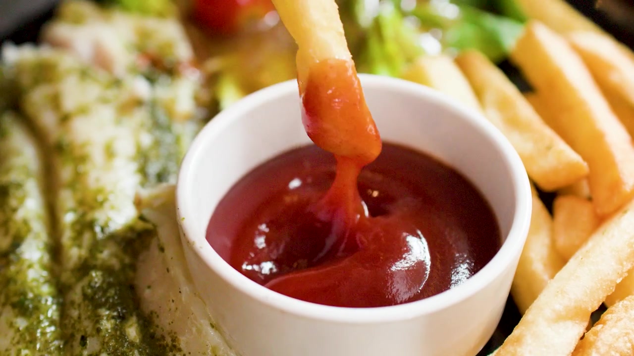 Nahaufnahme einer Hand, die eine goldene Pommes frites in rote Tomatenketchup-Soße tunkt.