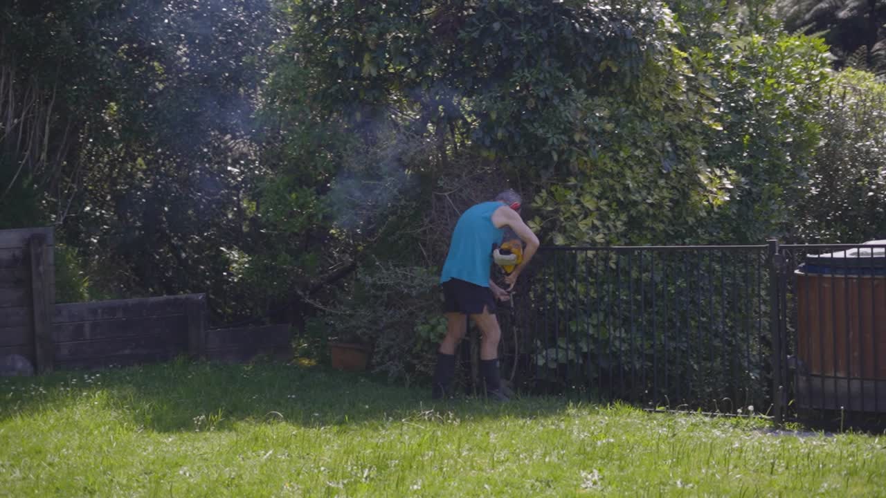 An Old Man Cutting Grass Using A Manual Grass Cutter At The Backyard