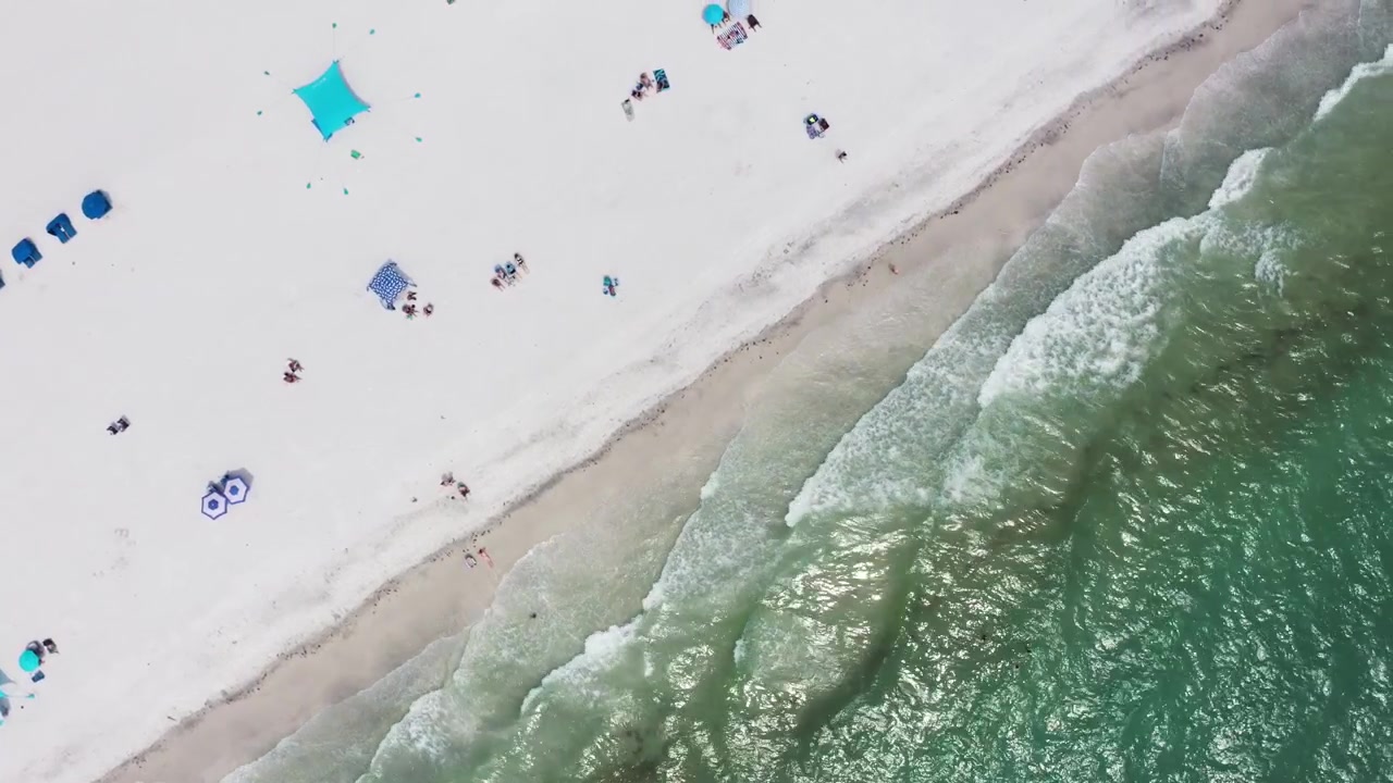 Aerial perspective of a sunlit beach with people relaxing and gentle surf approaching the shore. Ideal for vacation and leisure-themed content.