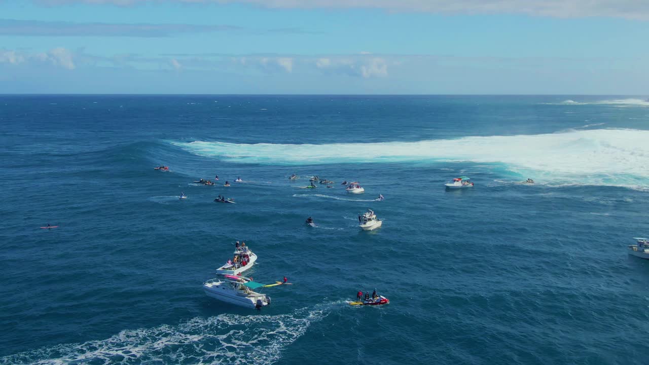 Surfers paddle with surfboard near big waves trying to ride at the right moment followed by rescue boats in Hawaii