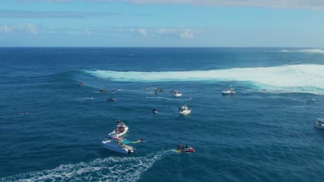 Surfers paddle with surfboard near big waves trying to ride at the right moment followed by rescue boats in Hawaii