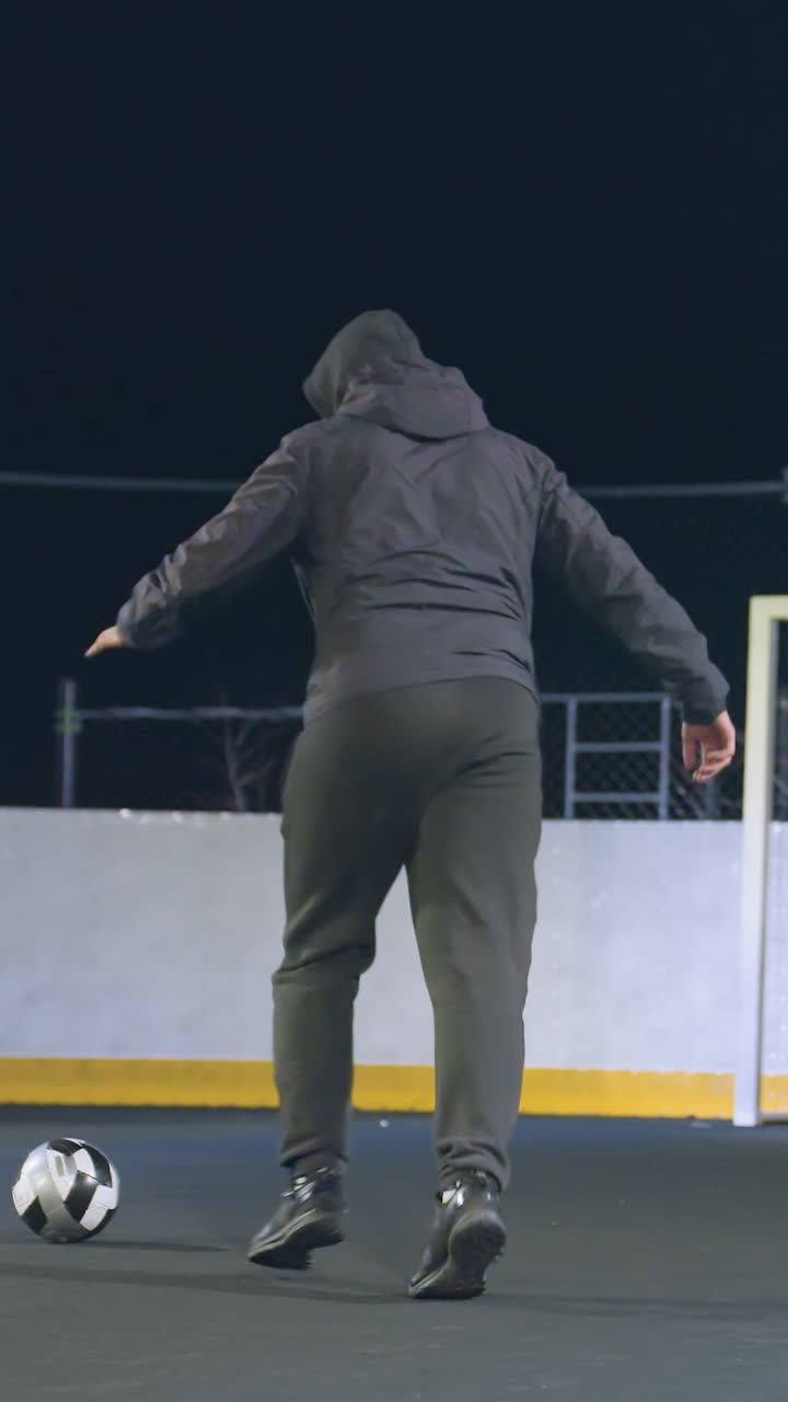 Athlete kicks soccer ball toward goalpost during night training on urban outdoor field as ball bounces out, illuminated backdrop and dynamic motion create an atmosphere of focus