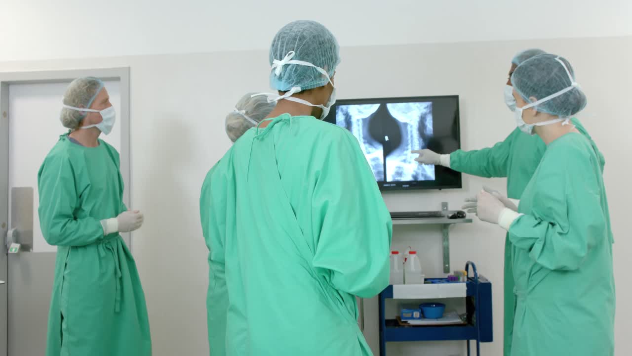Diverse surgeons wearing surgical gowns looking at x-ray scans in operating theatre, slow motion