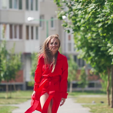 happy young woman in the street. beautiful young lady in passionate red dress is running happily on the city building background. slow motion.