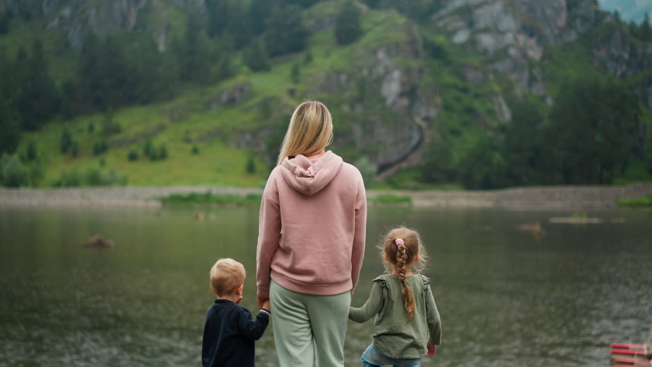 여자 는 아이 들 의 손 을 들고 고원 에서 조용 한 강 을 바라보고 있다