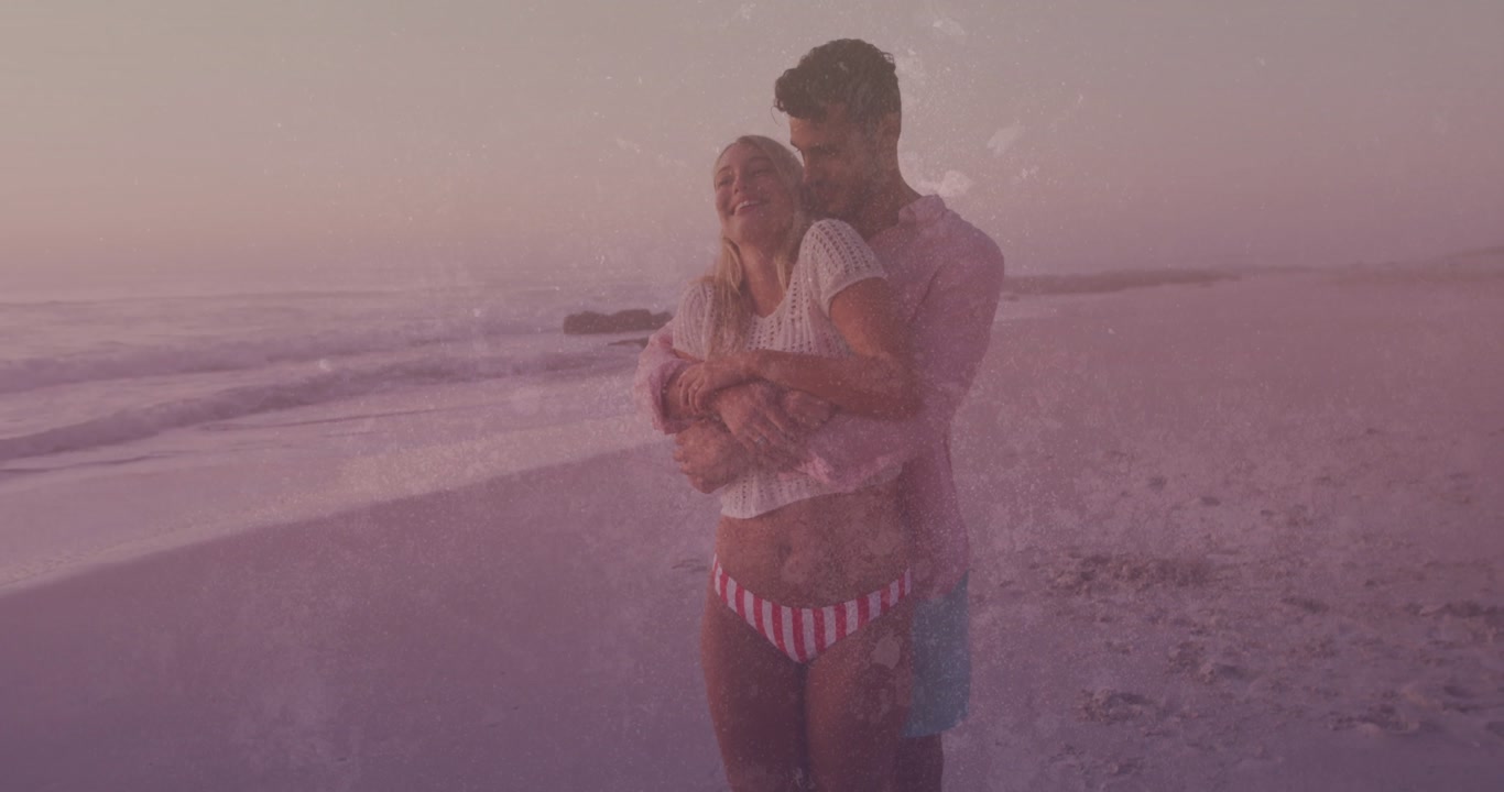 As water-splatter overlay drifts, man wrapping arms around woman standing at beach promoting health