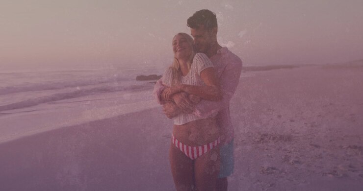 As water-splatter overlay drifts, man wrapping arms around woman standing at beach promoting health