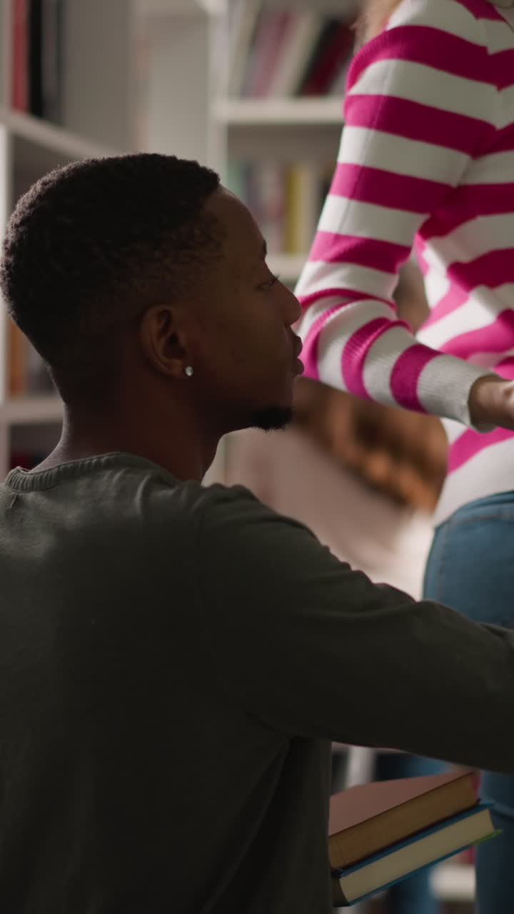 hombre negro toma libros de su amiga en la biblioteca. mujer joven de pie en la escalera de escalera alcanza el folio al tipo en la librería. estudiantes eligen libros de texto