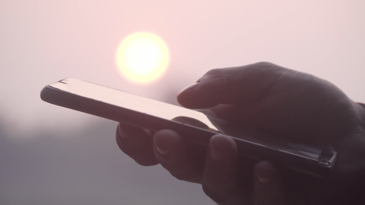 Side View. Hands of a man using smartphone during sunset, scrolling screen.