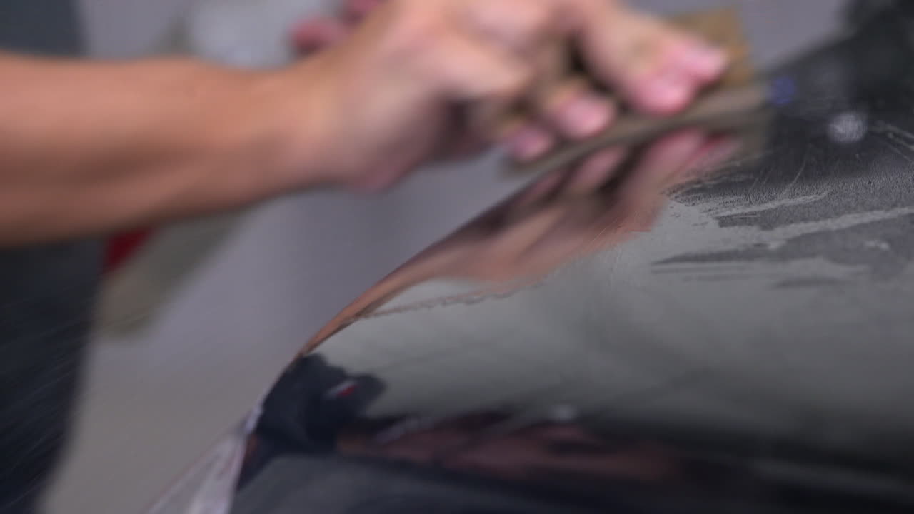 Close-up of spraying a car with slip solution while applying a paint protection film on a black car.