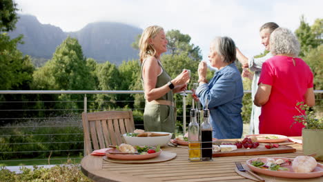 Un-Grupo-Diverso-De-Mujeres-Disfruta-De-Una-Comida-Al-Aire-Libre,-Con-Un-Telón-De-Fondo-Montañoso.