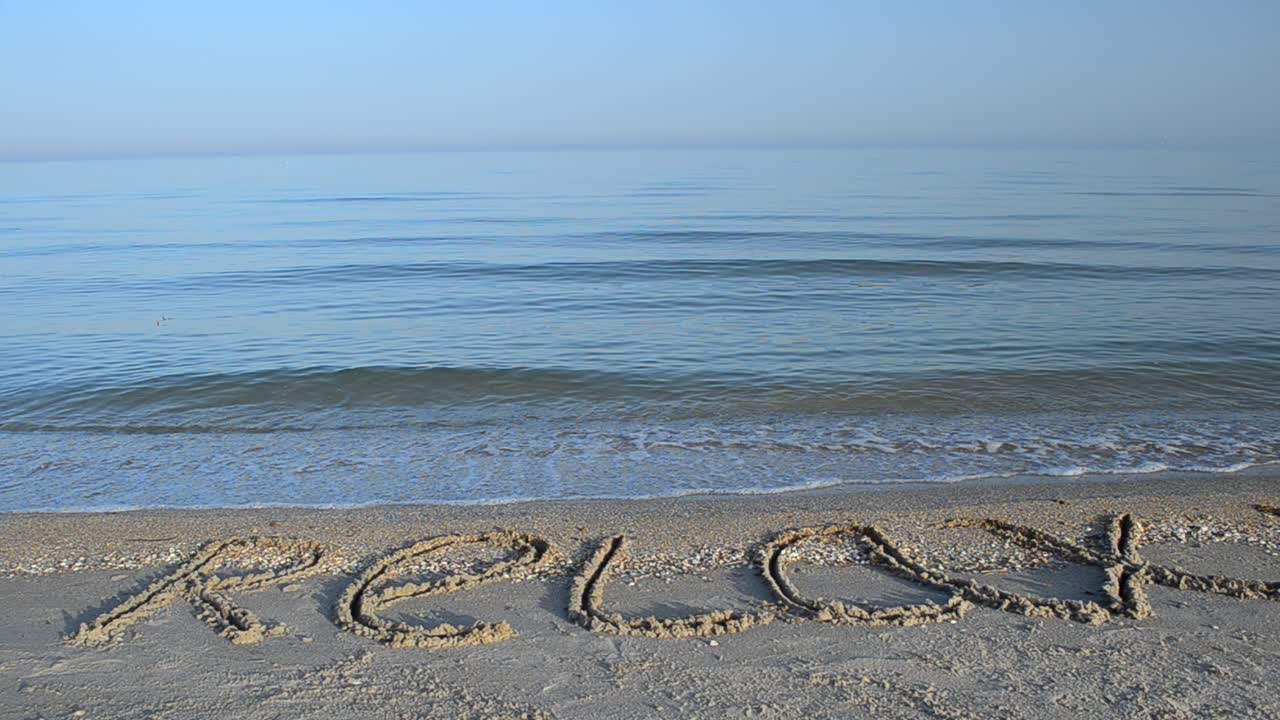 Indskrift med 'slap af' i sandet på stranden.