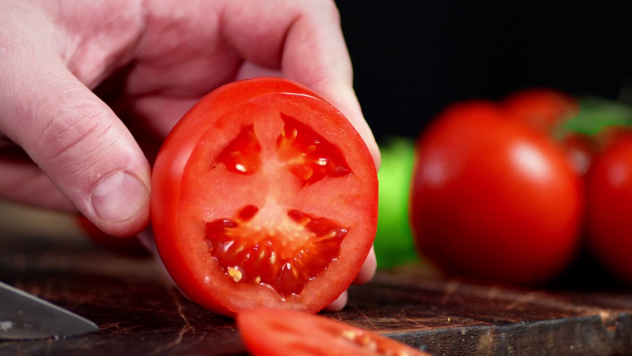 The hand of a man with a knife cut a fresh tomato.