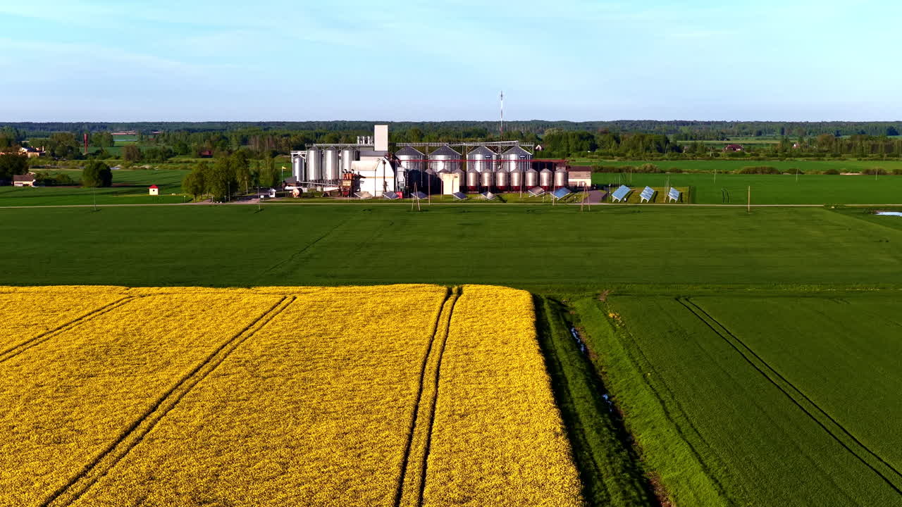 Large farm silos with solar panels beside green fields and yellow blooming crops