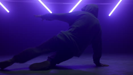 un desconocido realizando movimientos de hip-hop bajo la iluminación de neón. b-boy bailando en el suelo.