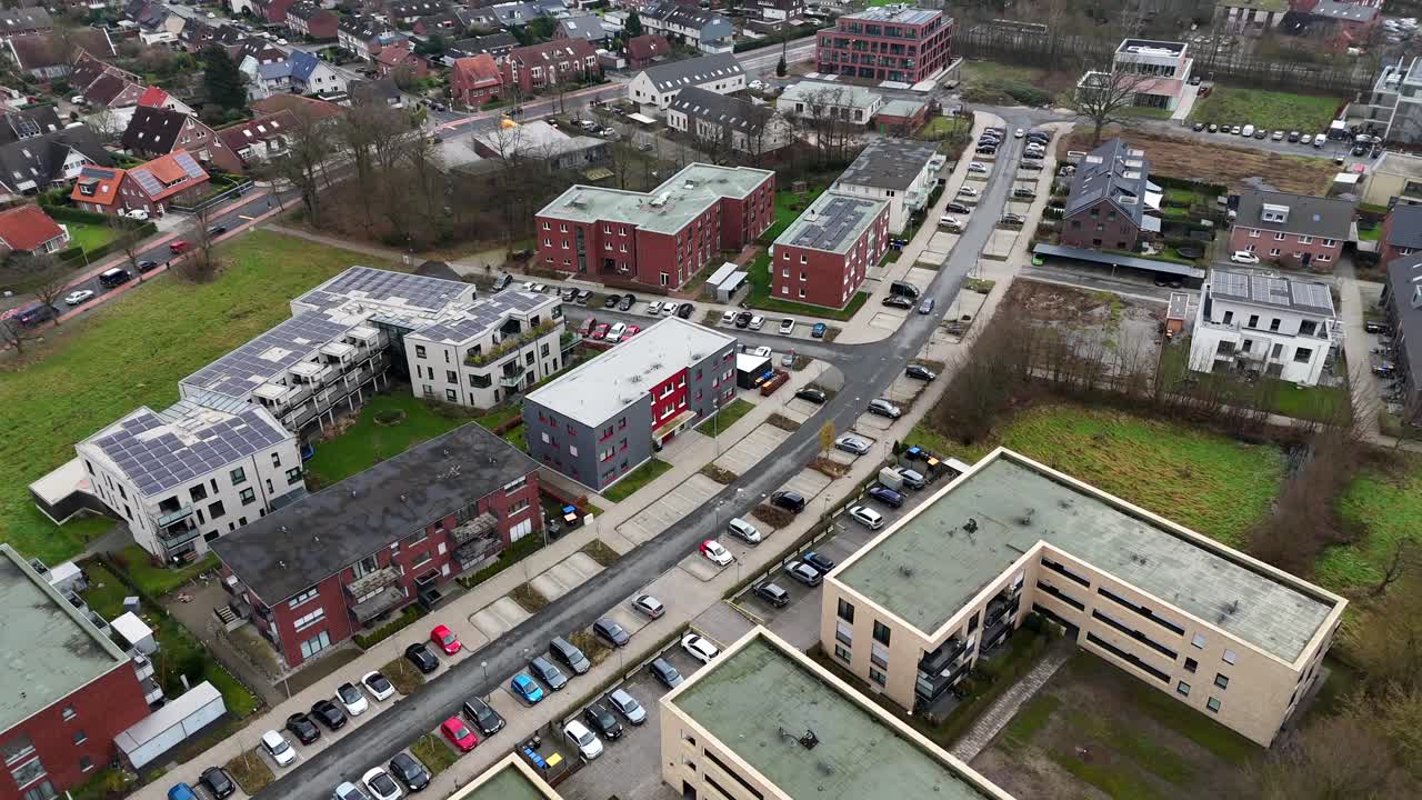 Modern residential apartments with solar panels on roof during cloudy day in winter. Parking cars on street. Aerial top down flyover. Architecture design in Germany.