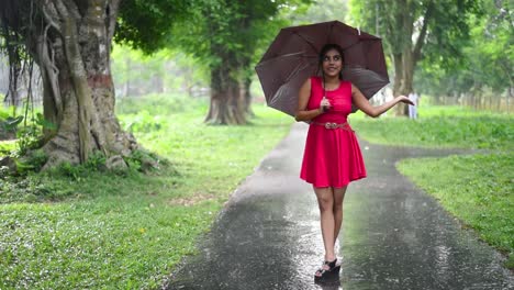 una hermosa y romántica chica asiática siente las gotas de lluvia en sus manos extendiendo sus manos fuera de su paraguas al aire libre