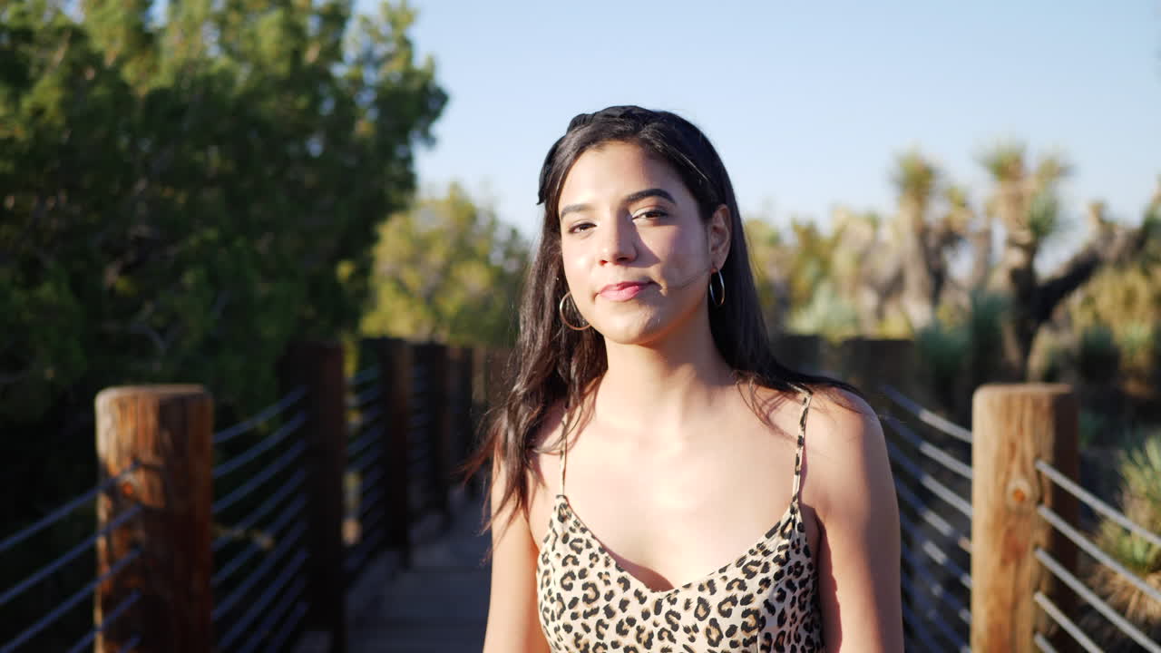 A beautiful young hispanic woman traveler walking and smiling on a nature path in slow motion in sunset light
