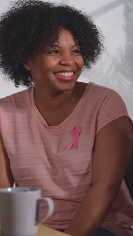 vertical video of smiling mid adult woman wearing pink breast cancer awareness ribbon meeting and talking at therapy support group for cancer treatment patients with counsellor 1