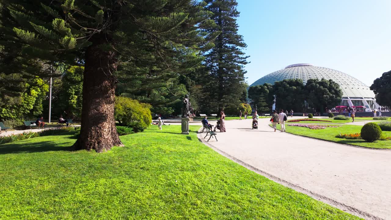 People enjoying a sunny day in a park near a large dome in Porto