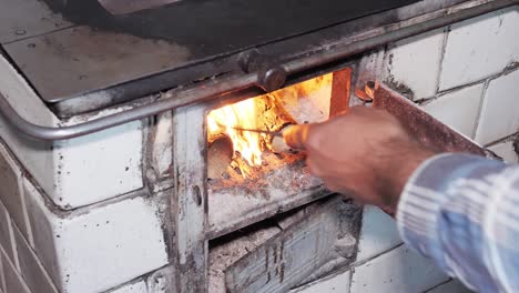 el hombre usa un póquer para nivelar la madera y un hogar en una cocina rústica antigua