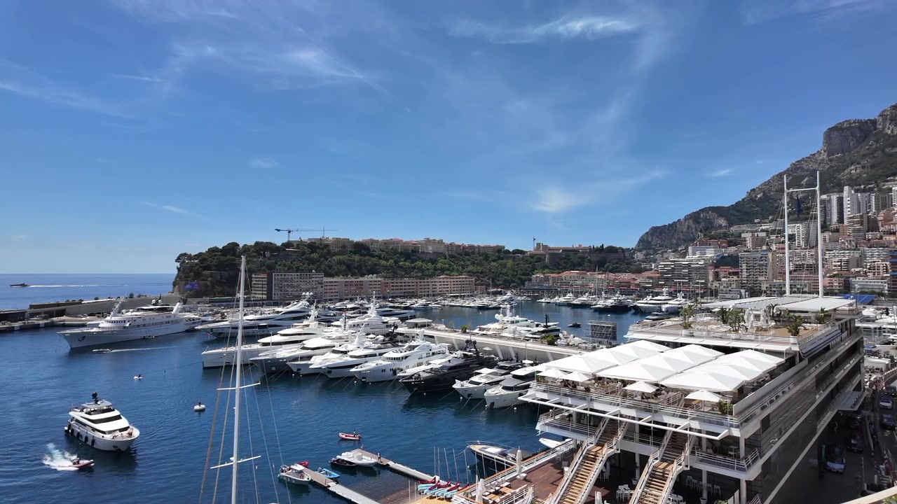 Yacht di lusso ormeggiati nel Port Hercule di Monaco sotto un cielo azzurro limpido, con il lungomare di Monte Carlo e le colline circostanti che creano un'elegante scena di viaggio e stile di vita mediterraneo.