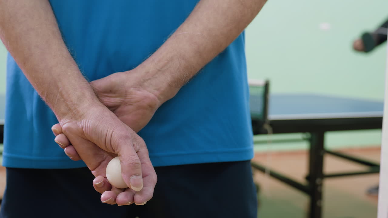 Close up of senior coach hand holding table tennis ball behind back during indoor practice session, highlighting discipline, preparation, focus, and readiness in concentrated