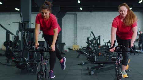 Grupo-De-Mujeres-Atléticas-Montando-En-Rutina-De-Entrenamiento-De-Bicicleta-Estacionaria-Giratoria-En-El-Gimnasio,-Pérdida-De-Peso-En-Interiores