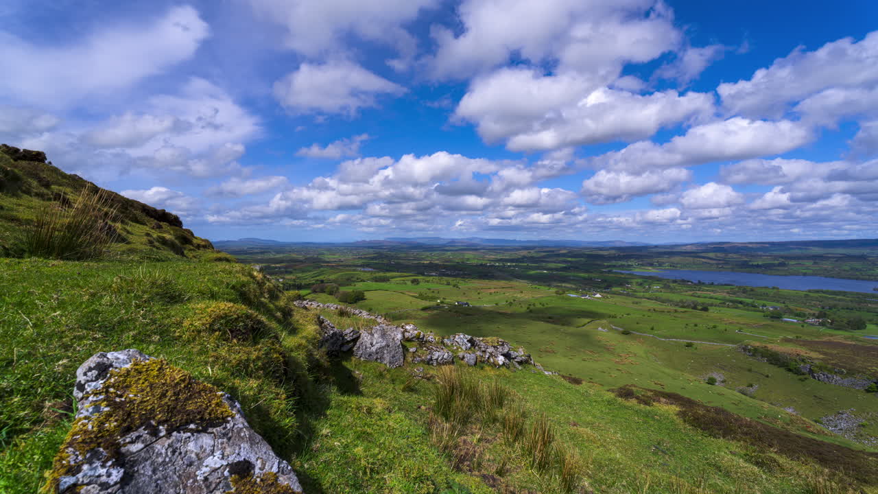 Timelapse af landligt landskab med klippeformation i forgrunden samt bakker og sø i det fjerne p en solrig, skyet dag set fra Carrowkeel i County Sligo i Irland