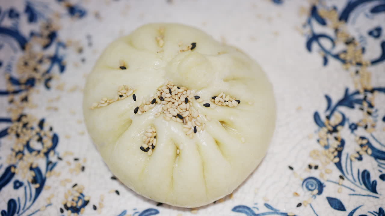 Close up of a steamed bun topped with sesame seeds on a decorative ceramic plate