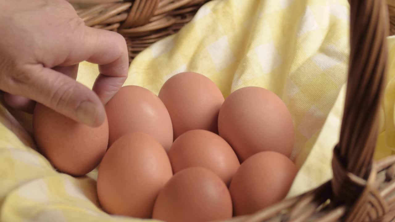Mão colocando ovos marrons frescos em uma cesta de vime.
