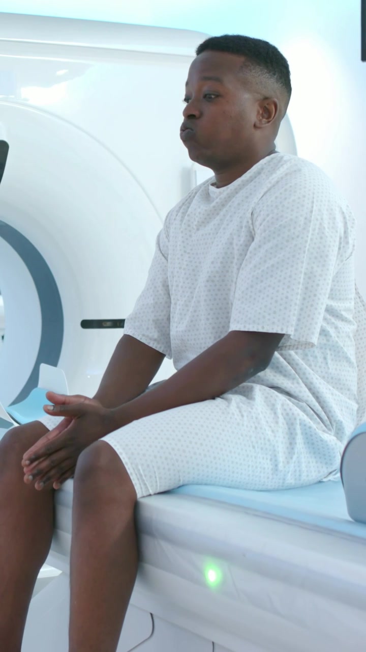 Video verticale: Paziente maschio seduto che trattiene il respiro con un monitor che segnala vicino allo scanner, in camice