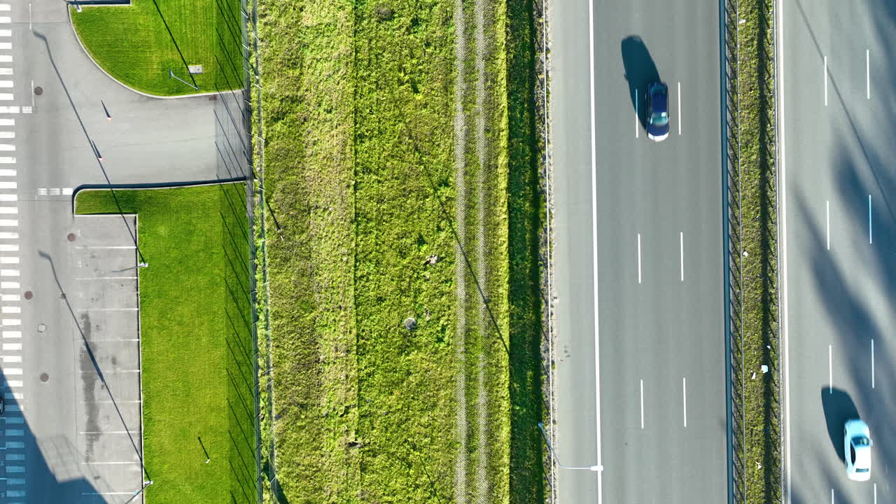 Aerial top‑down shot showing a parking lot beside a grassy divider and multi‑lane highway with a single moving car