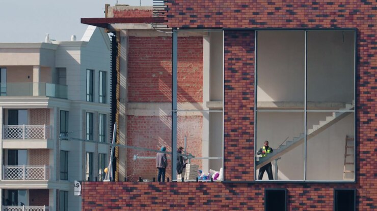 Trabajadores dentro de un edificio moderno en construcción con paredes de ladrillo visto, interiores sin terminar y grandes aberturas para ventanas.