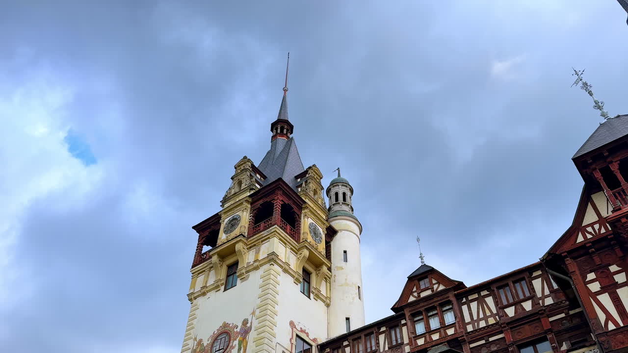 Clock tower of a beautiful Peles Castle in Sinaia, Romania. Low angle view at the steeple of the building at the backdrop of cloudy sky